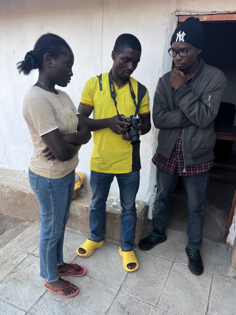 Three individuals discussing a camera in a casual setting. The person in yellow is holding a camera while the others observe attentively.