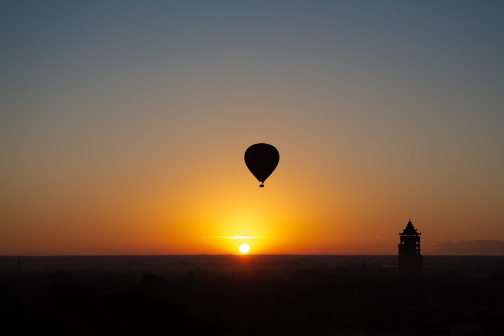 Silhouette of a hot air balloon against a vibrant sunset, with a tower visible in the foreground.